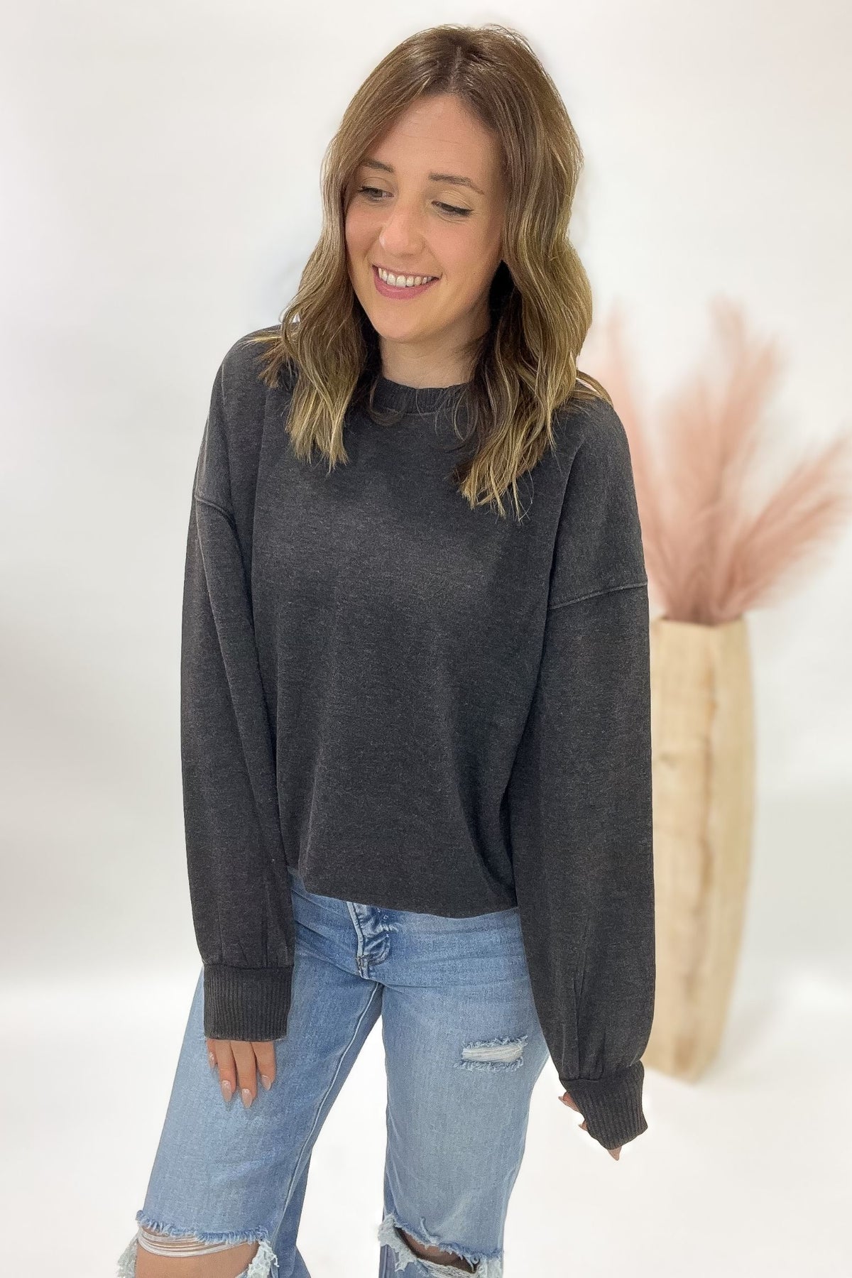 Woman wearing a acid wash black sweatshirt and light blue jeans against a white background