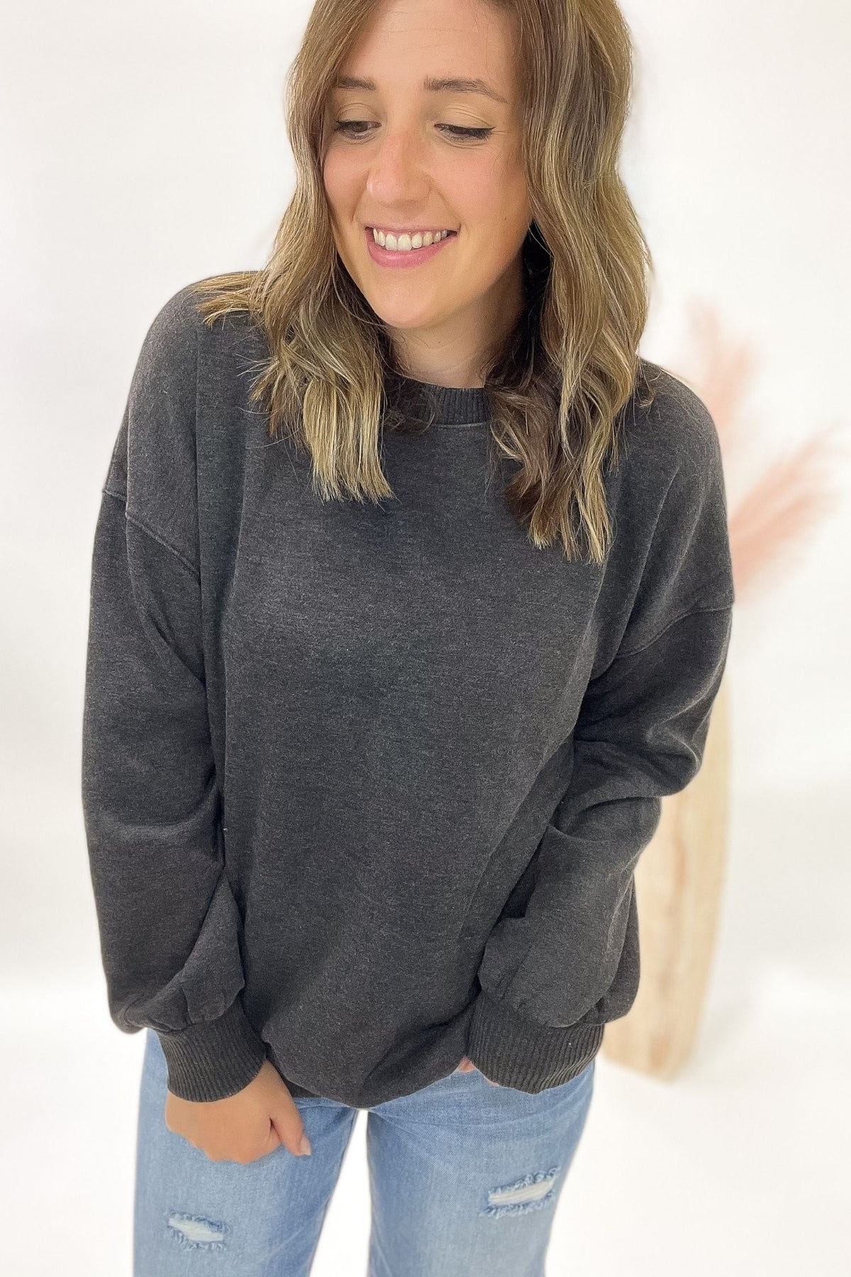 Woman wearing a acid wash black sweatshirt and light blue jeans against a white background