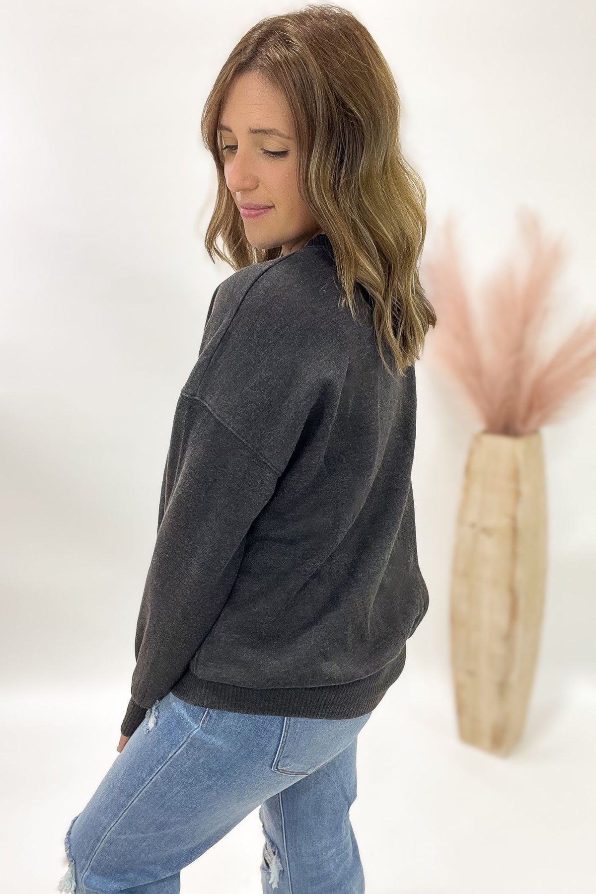 Woman wearing a acid wash black sweatshirt and blue jeans against a white background
