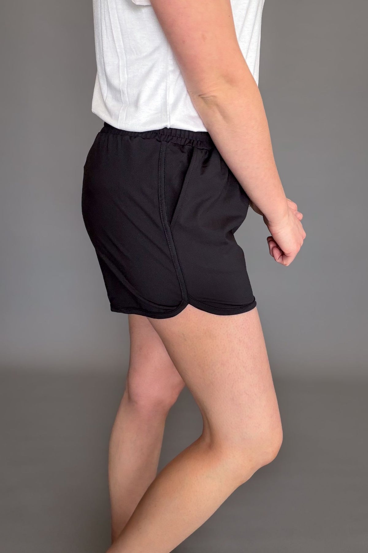 Black soft stretchy everyday shorts with drawstring waist and pockets styled with sneakers showing the side view