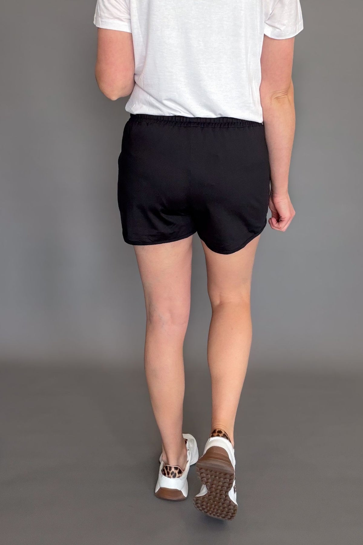 Black soft stretchy everyday shorts with drawstring waist and pockets styled with sneakers showing the back details