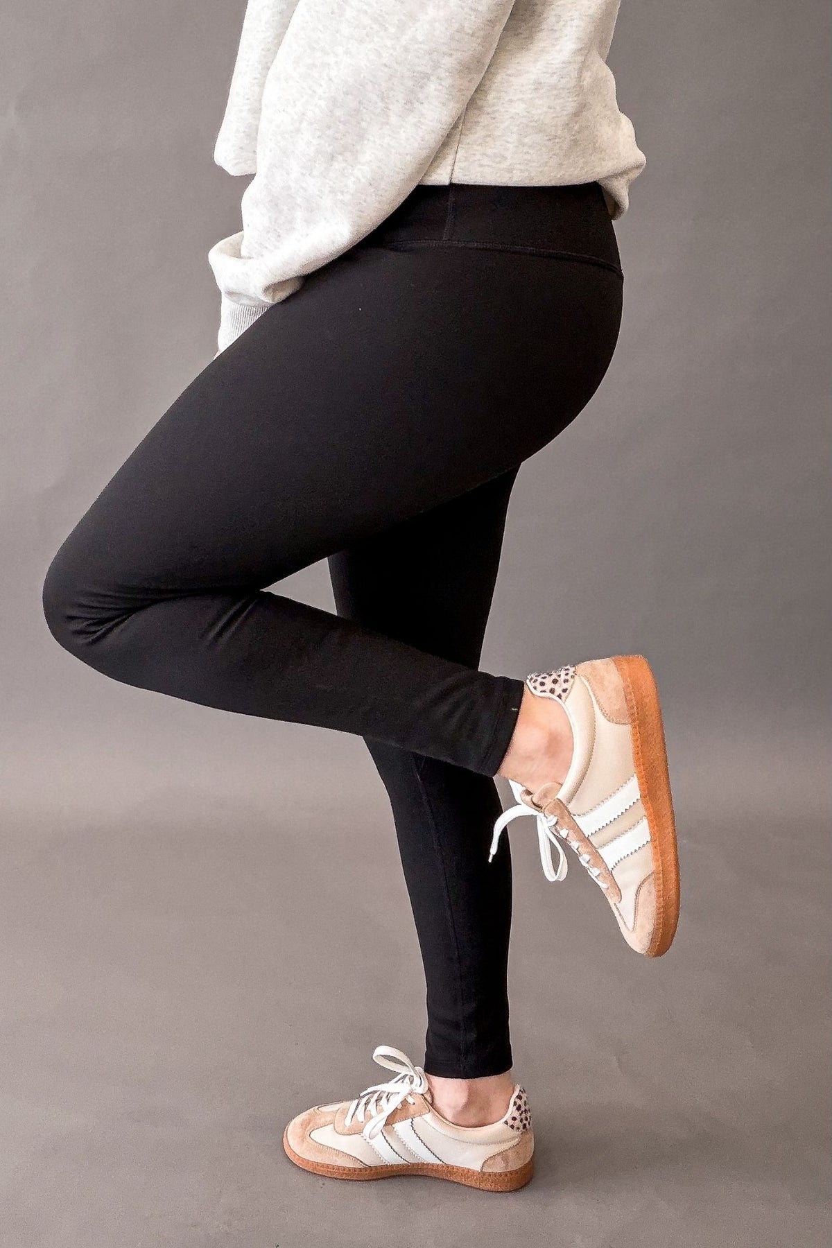 woman wearing black leggings with a heather grey top and sneakers on a grey background showing the side details