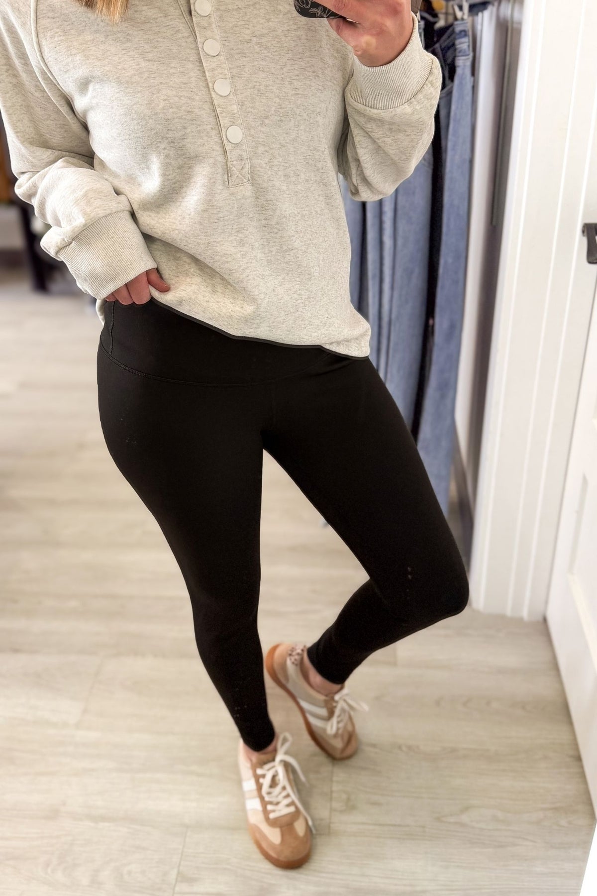 woman taking a mirror selfie showing woman wearing black leggings with a heather grey top and sneakers on a grey background.