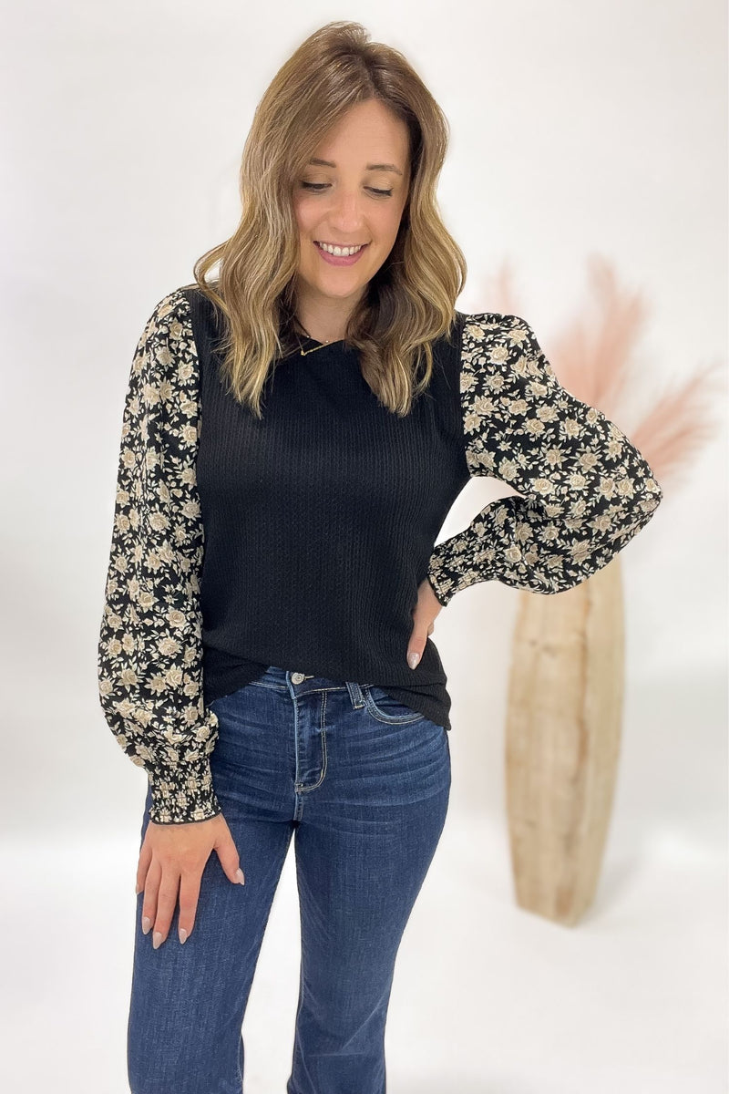 Woman wearing a black top with floral sleeves and blue jeans on a white background