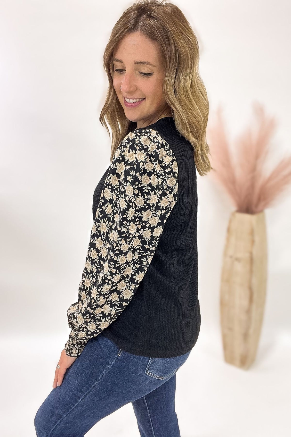 Woman wearing a black long-sleeve top with floral sleeves against a white background