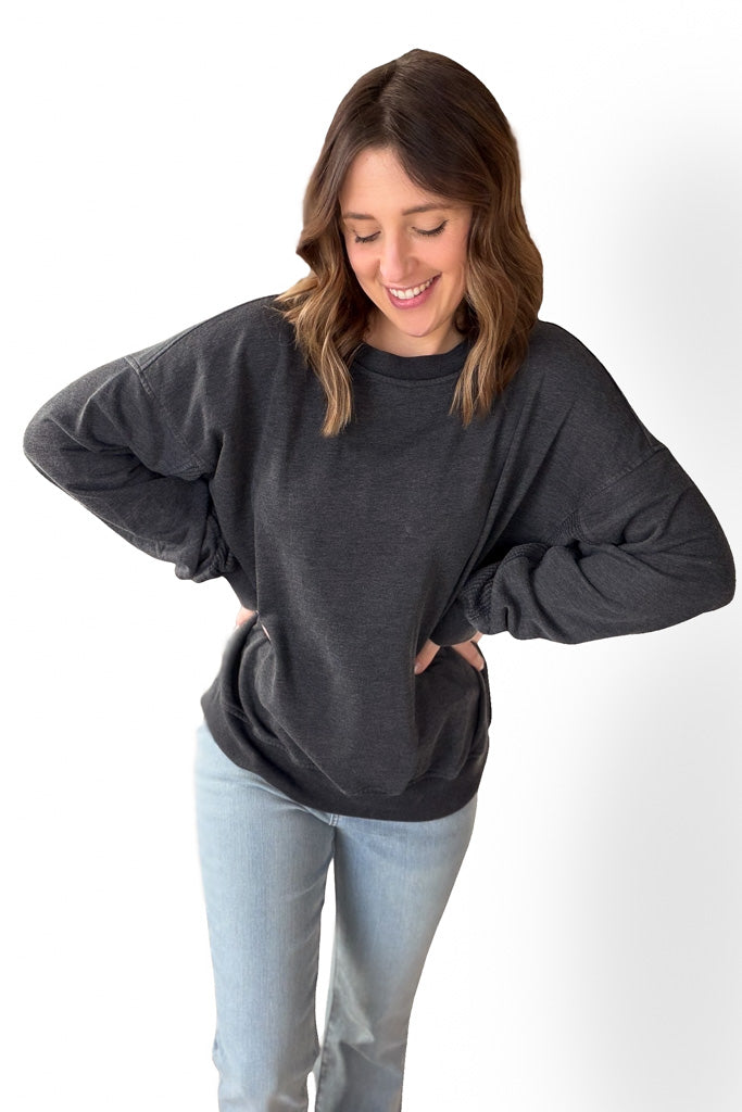 Woman wearing a dark gray oversized sweatshirt and light blue jeans on a white background