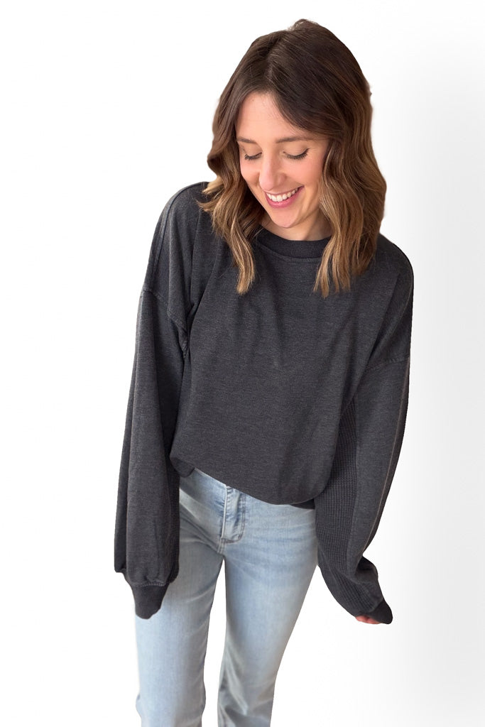 Woman wearing a dark gray long-sleeve sweatshirt and light blue jeans on a white background