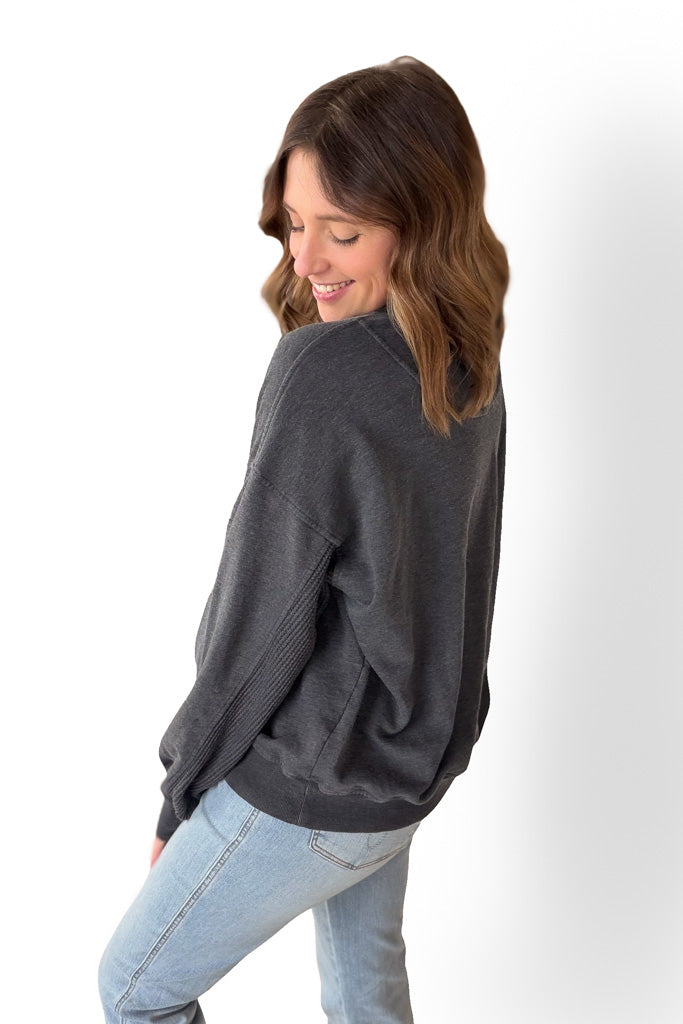 Woman wearing a dark gray sweatshirt and light blue jeans on a white background