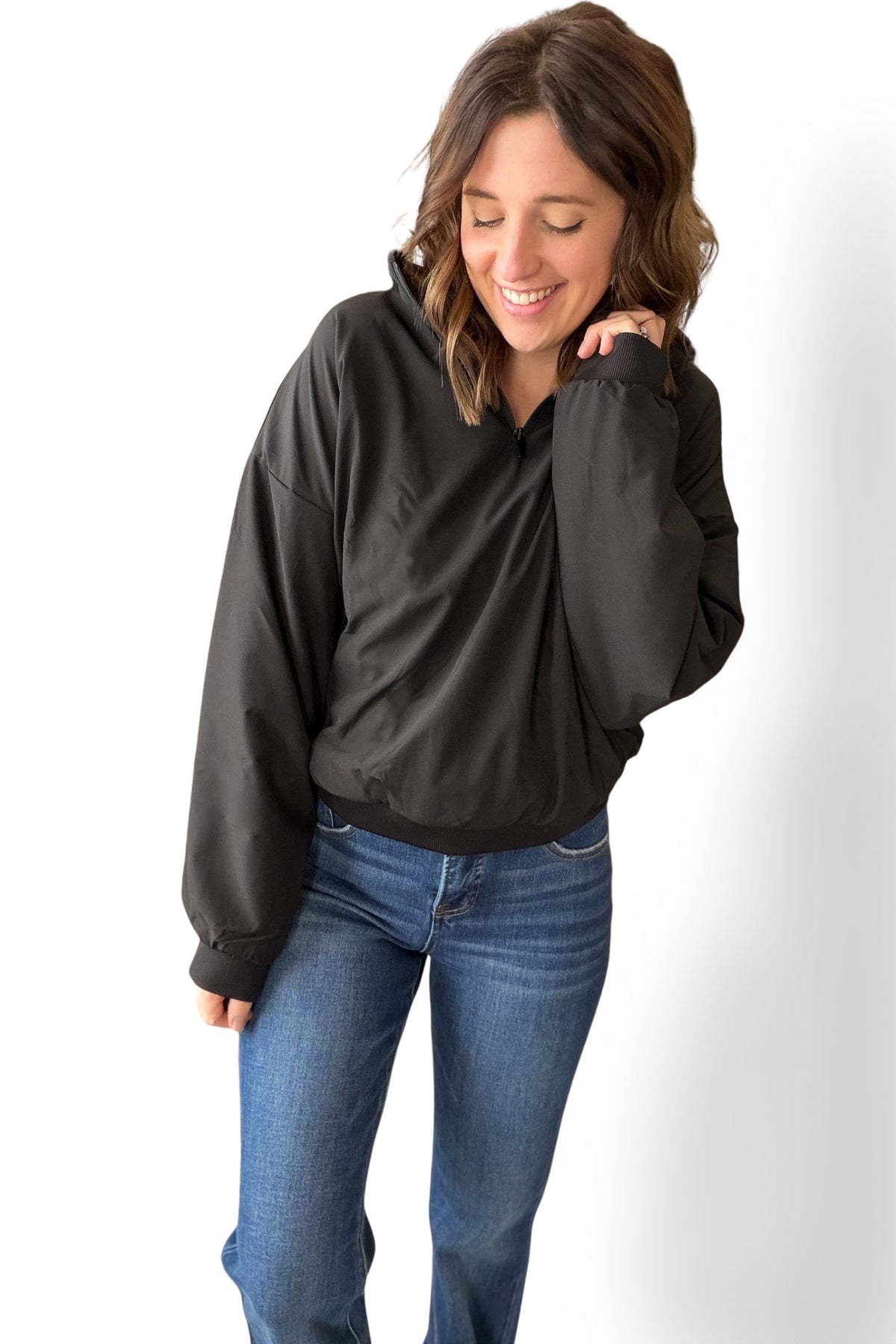 Woman wearing a black quarter zip and blue jeans on a white background