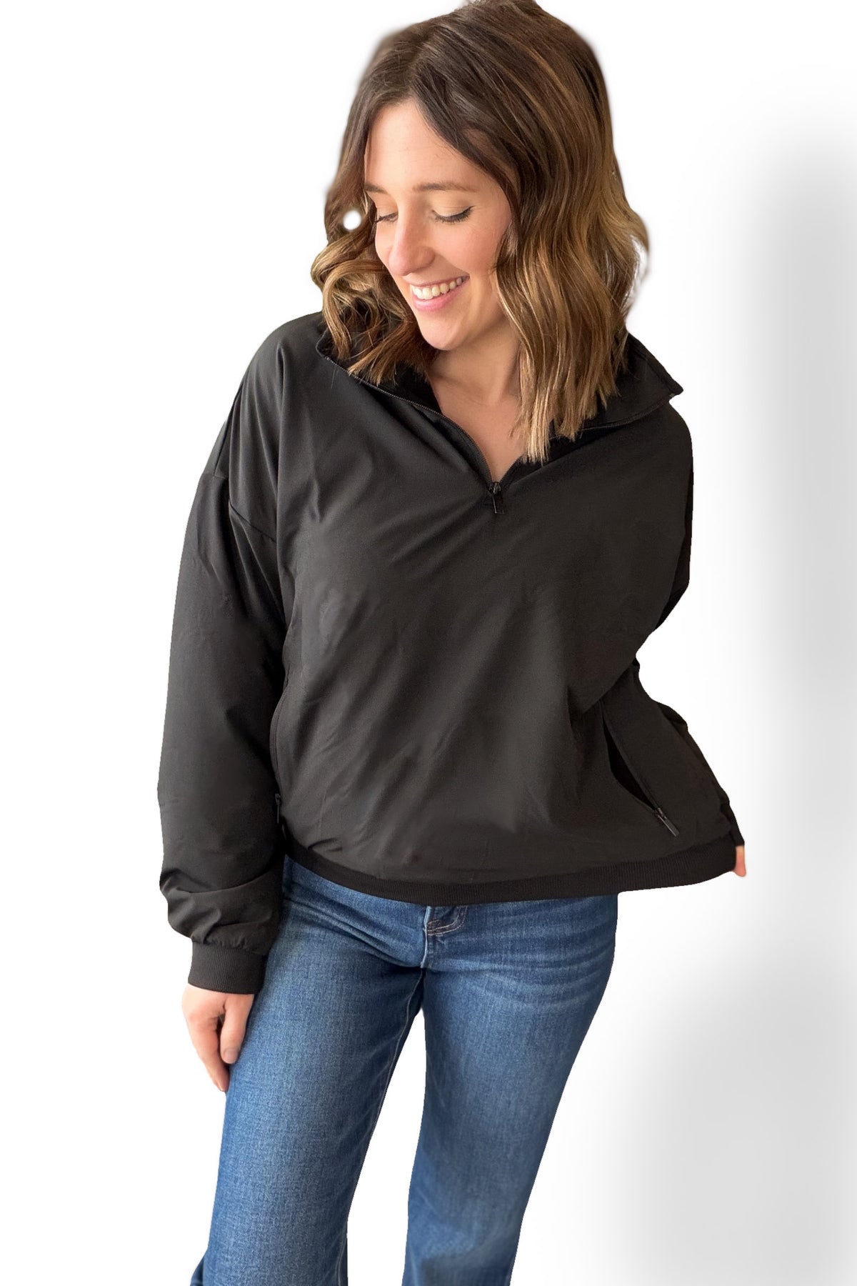 Woman wearing a black quarter zip and blue jeans on a white background