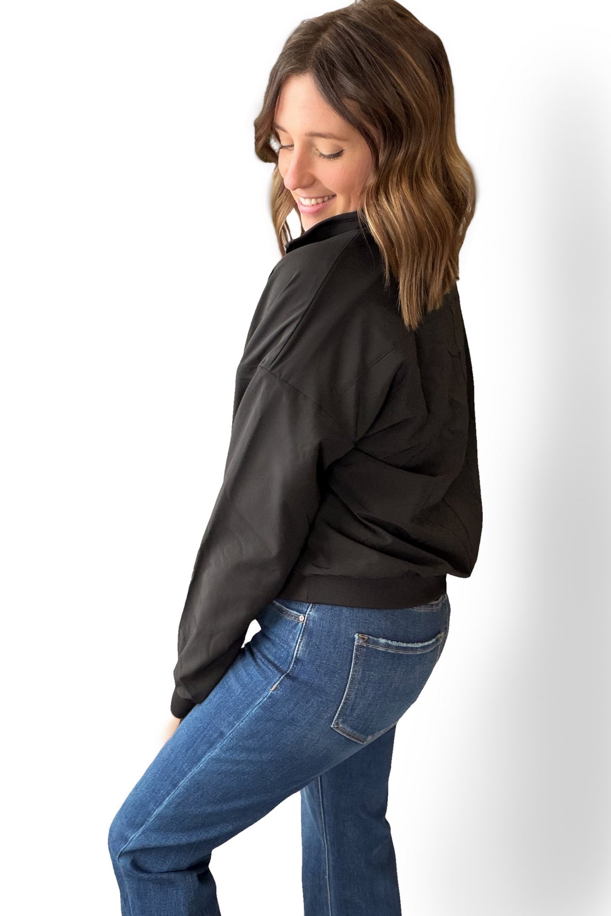 Woman wearing a black quarter zip and blue jeans against a white background