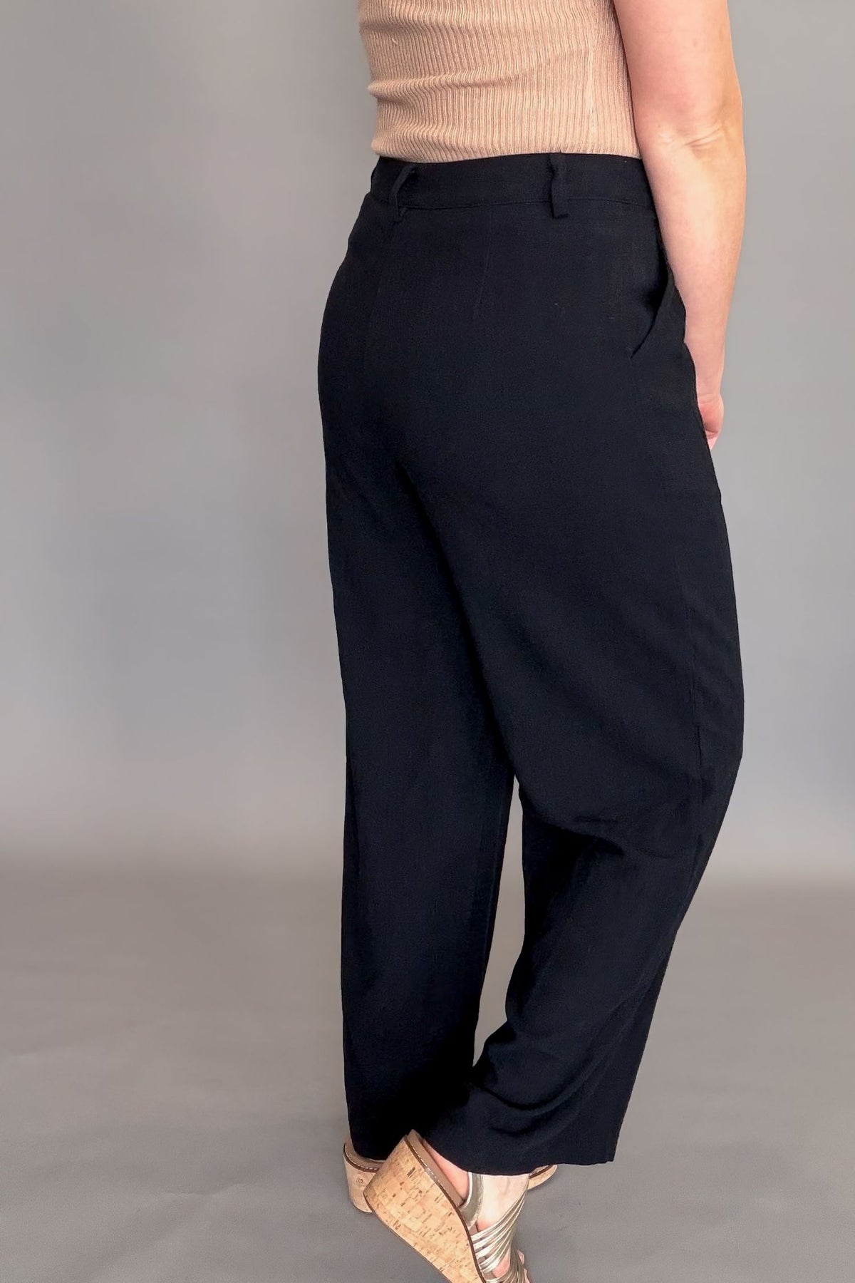 Person wearing black pants and a beige top on a gray background