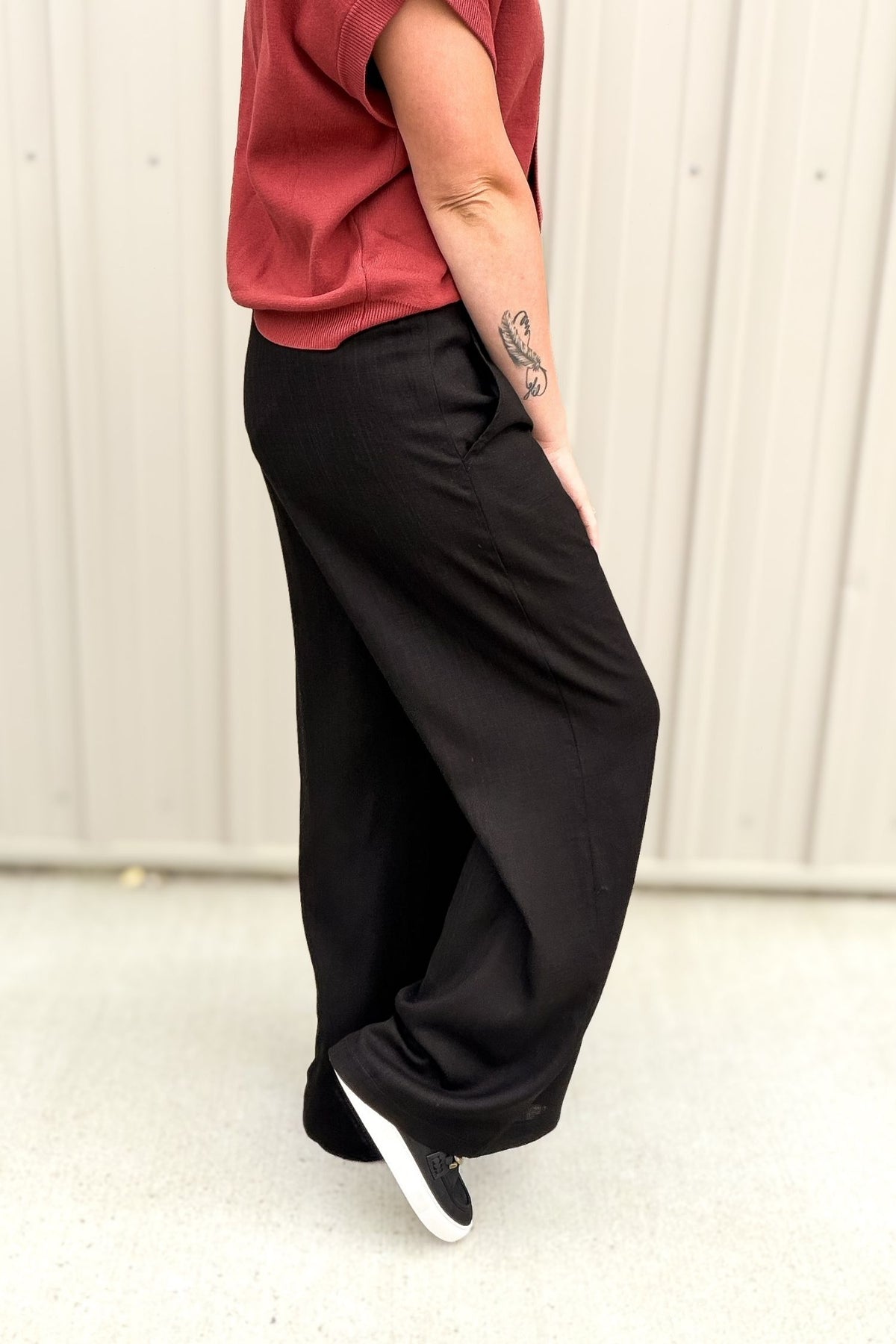 Person wearing a red shirt and black wide-leg pants against a white background