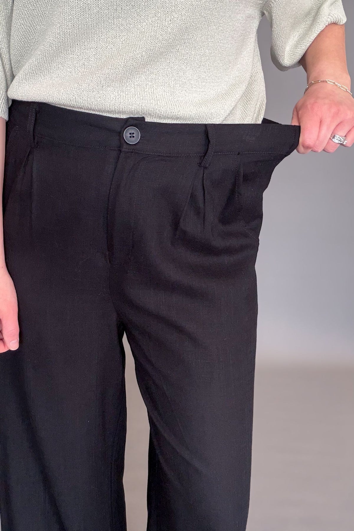 woman wearing a black linen blend wide leg work pant showing the stretch in the waistband