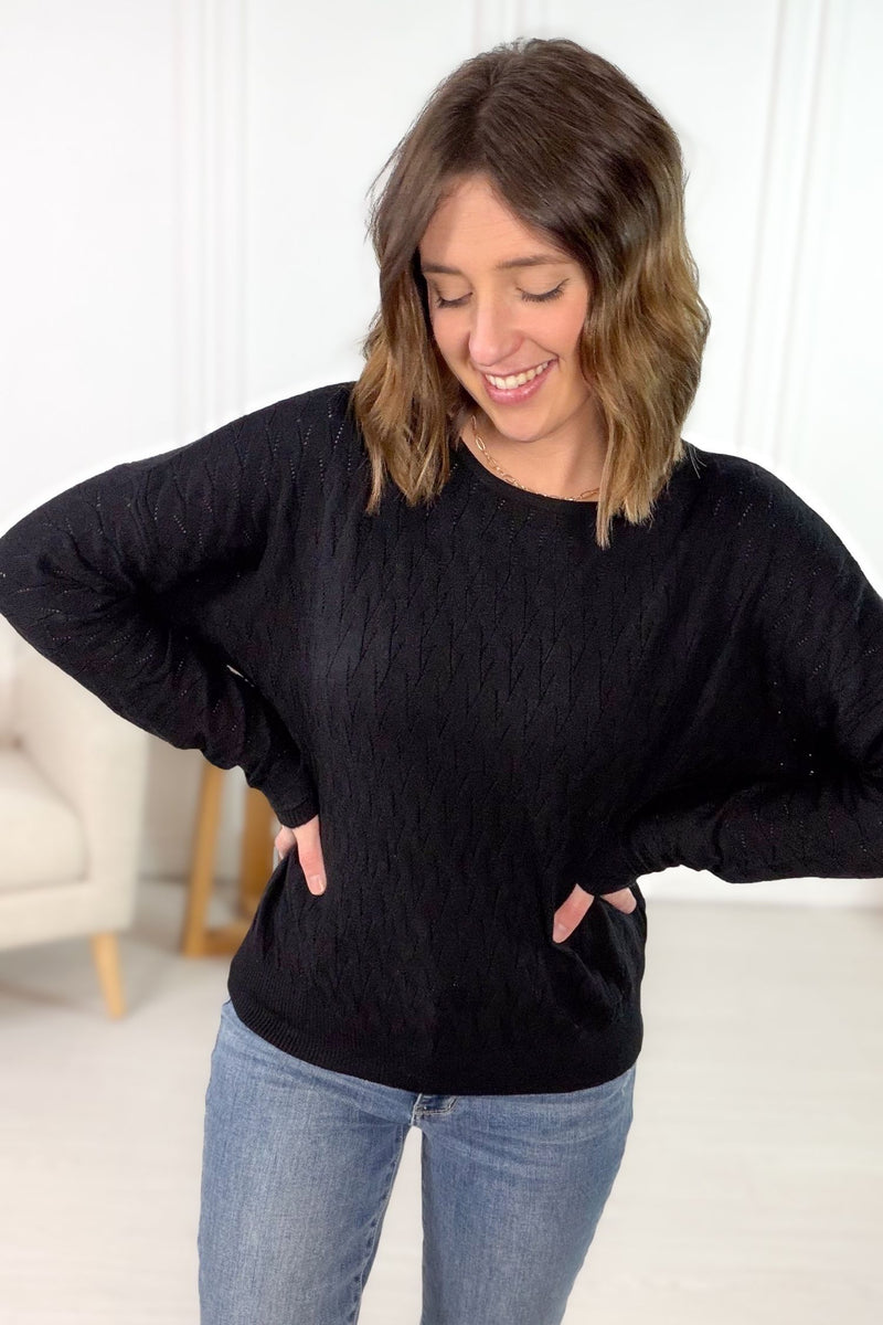Black pointelle dolman sleeve long sleeve top with textured open knit pattern styled with light wash denim.