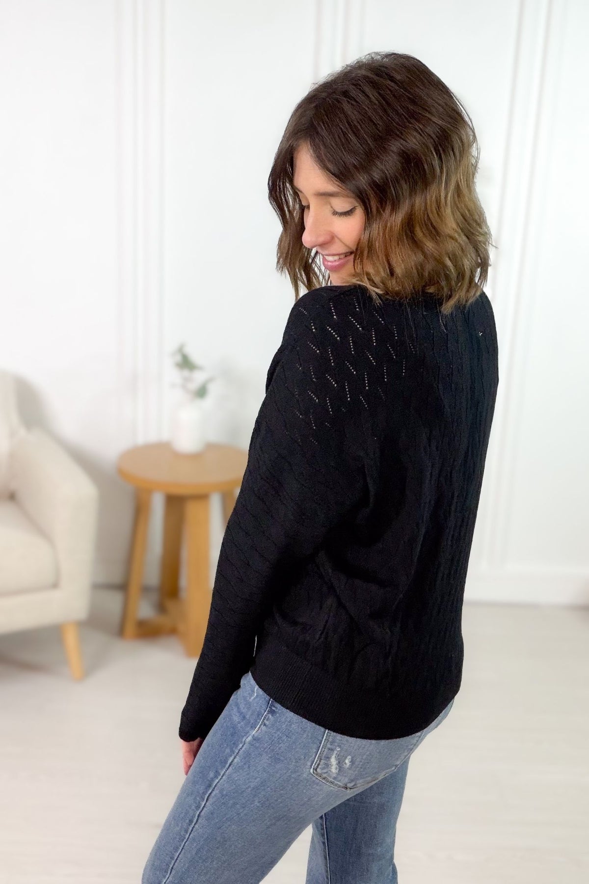 Black pointelle dolman sleeve long sleeve top with textured open knit pattern styled with light wash denim showing the side/back details.