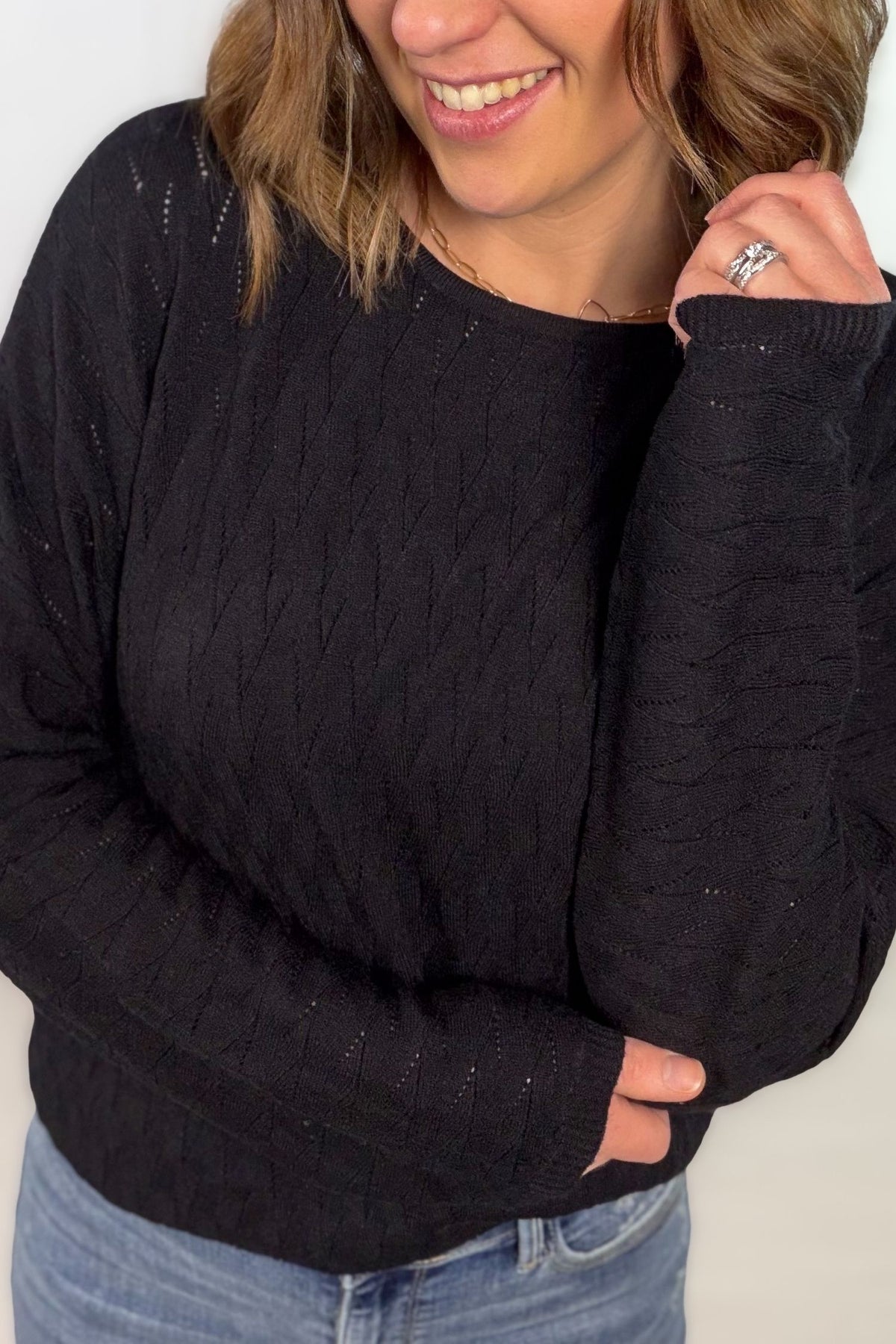 Black pointelle dolman sleeve long sleeve top with textured open knit pattern styled with light wash denim showing texture.