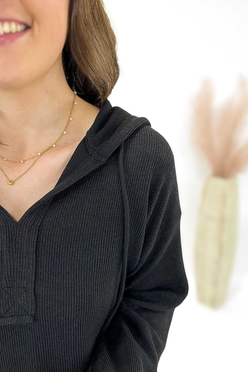 Woman wearing a black ribbed hoodie with a blurred background