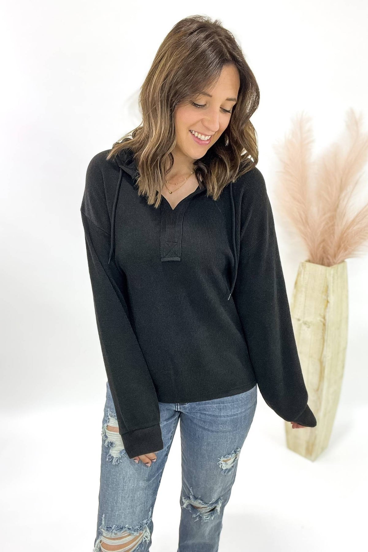 Woman wearing a black long-sleeve top and blue jeans against a white background