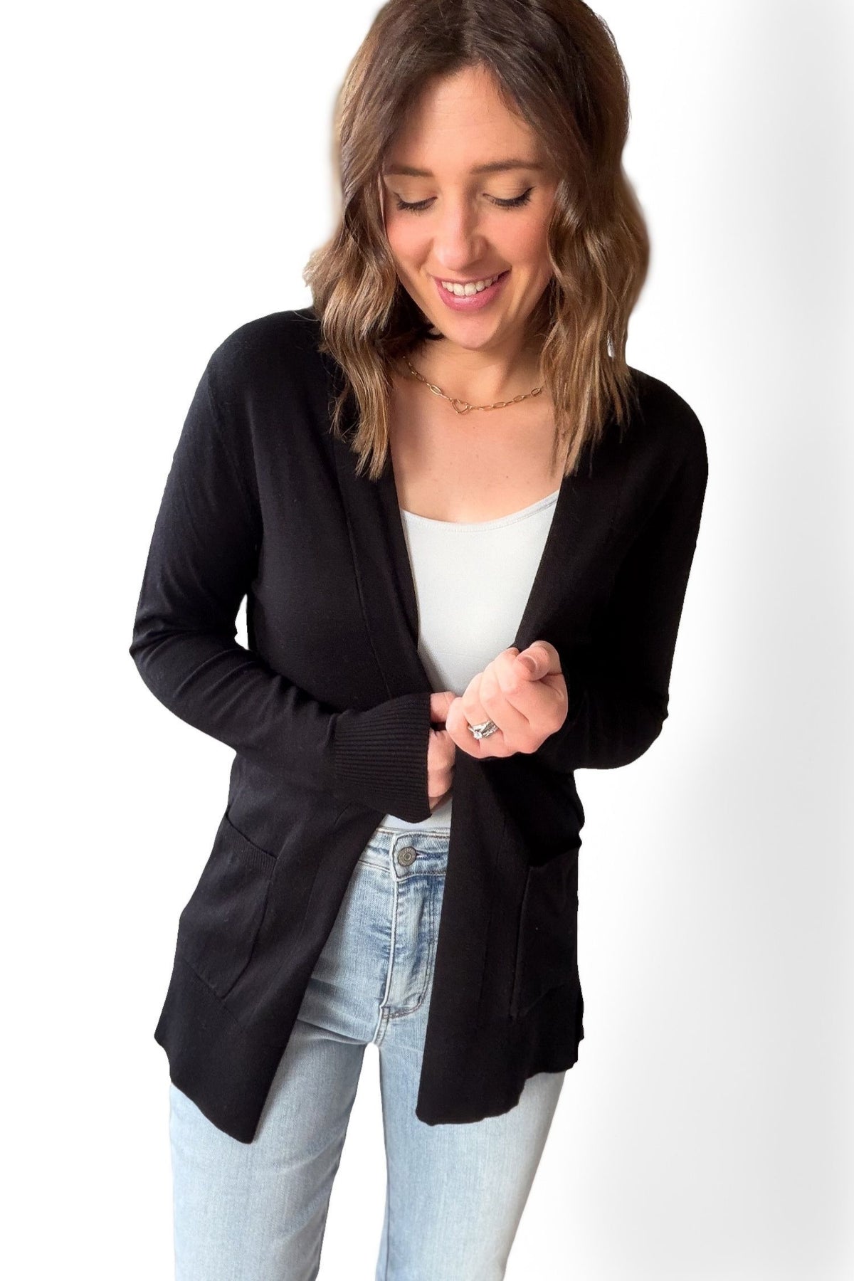 Woman wearing a black cardigan over a white top and light blue jeans on a white background