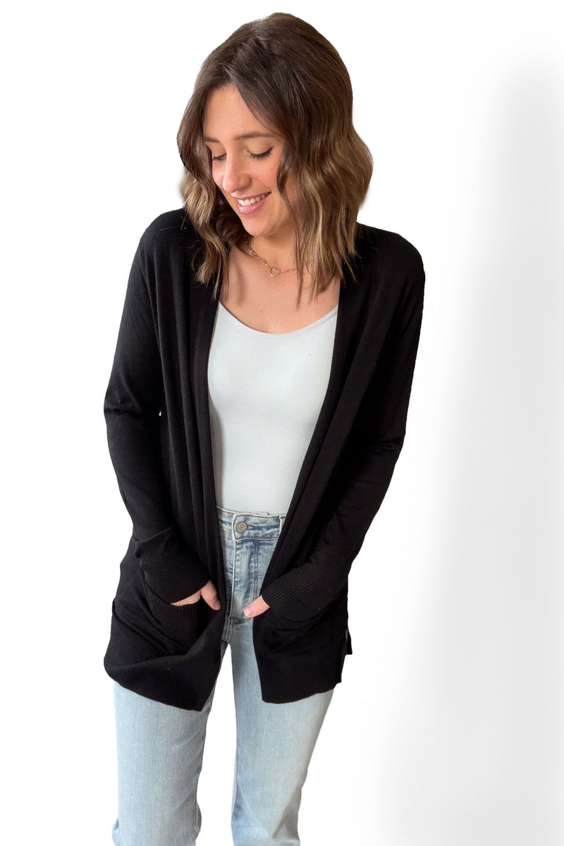 Woman wearing a black cardigan over a white top and light blue jeans on a white background