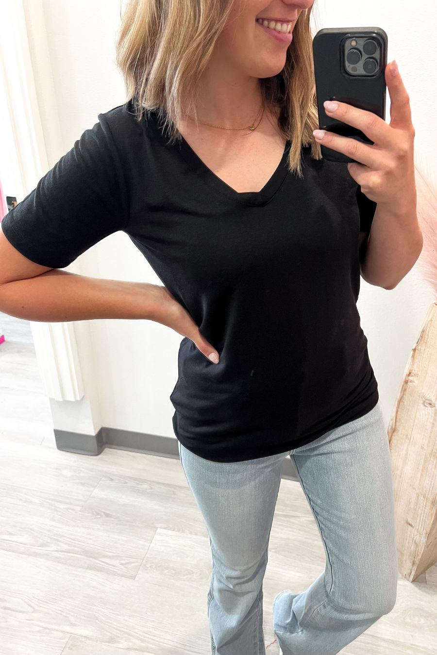 Person wearing a black t-shirt and light blue jeans, taking a mirror selfie.