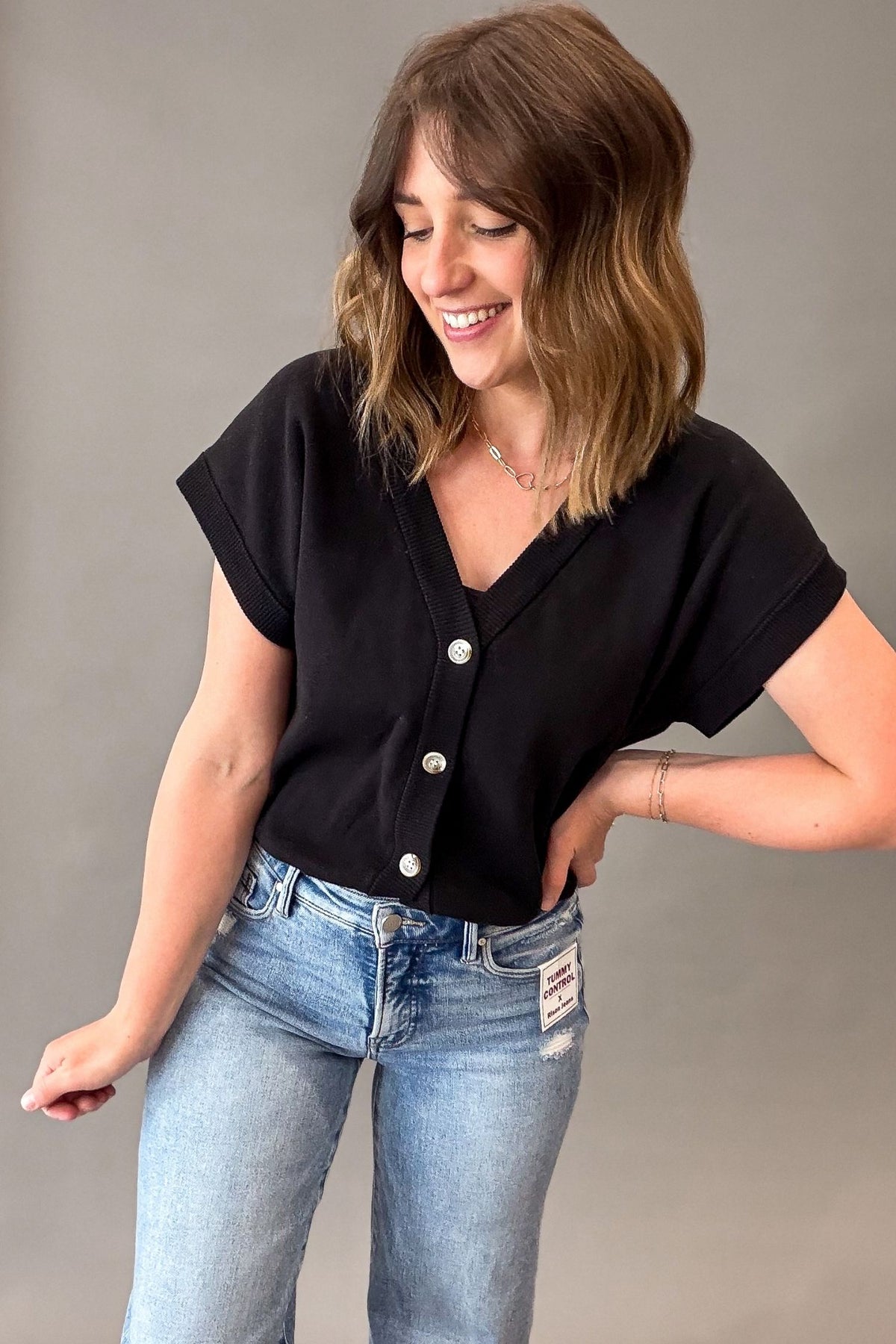 Woman wearing a black button-up shirt and light blue jeans against a gray background