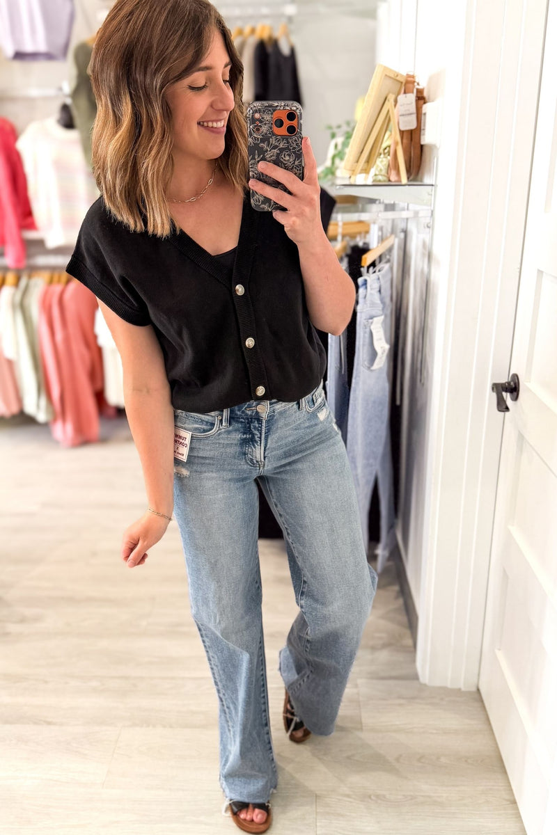 Woman taking a mirror selfie wearing a black top and blue jeans in a clothing store.