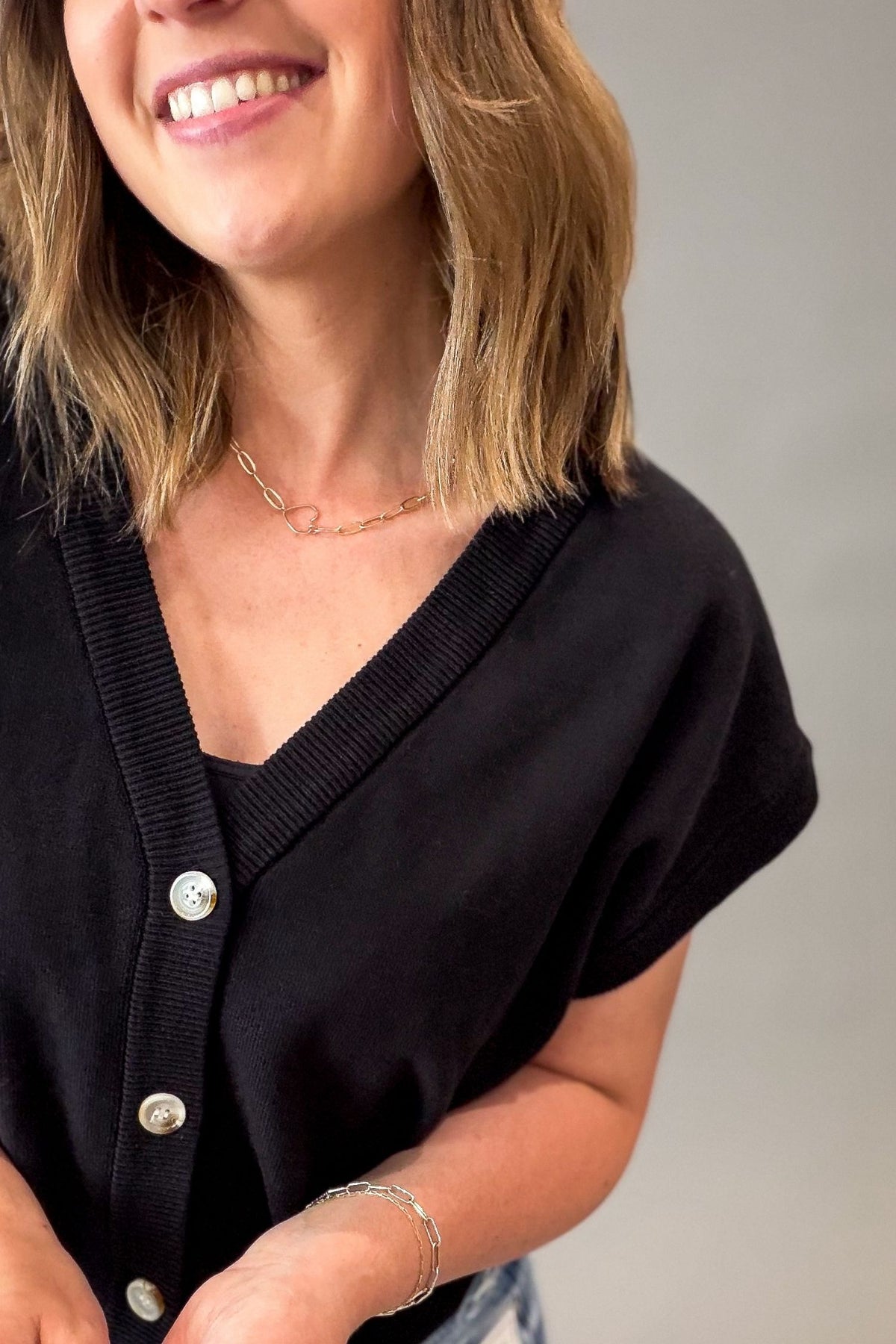Woman wearing a black cardigan with silver buttons on a neutral background