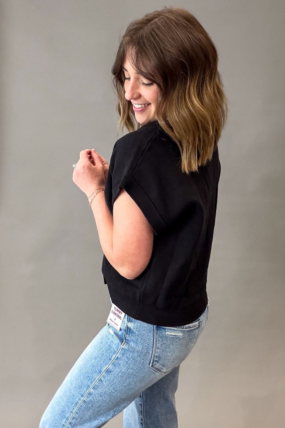 Woman wearing a black button front caridgan and blue jeans against a plain background