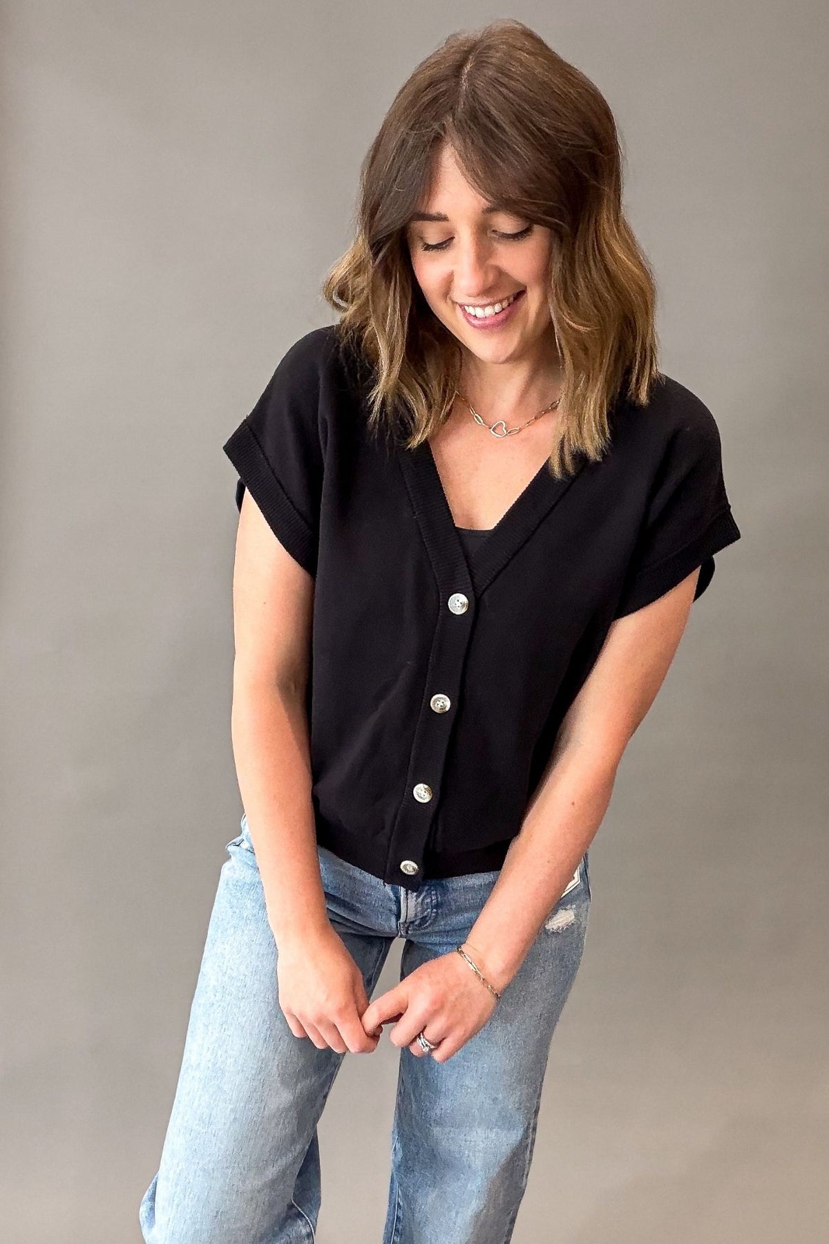 Woman wearing a black button-up shirt and blue jeans against a gray background
