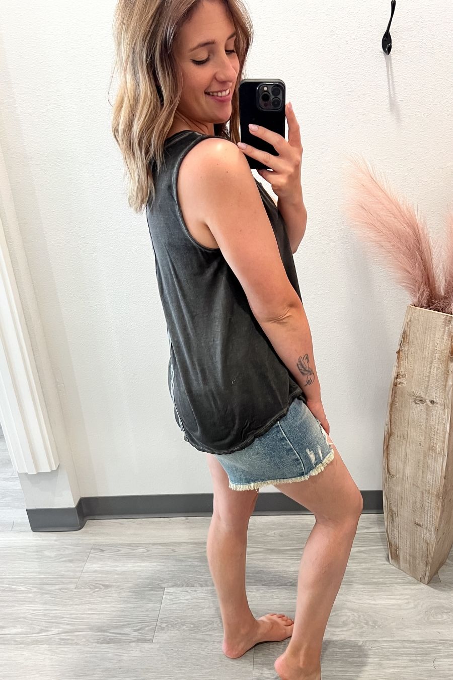Woman taking a mirror selfie wearing a black sleeveless top and denim skirt.