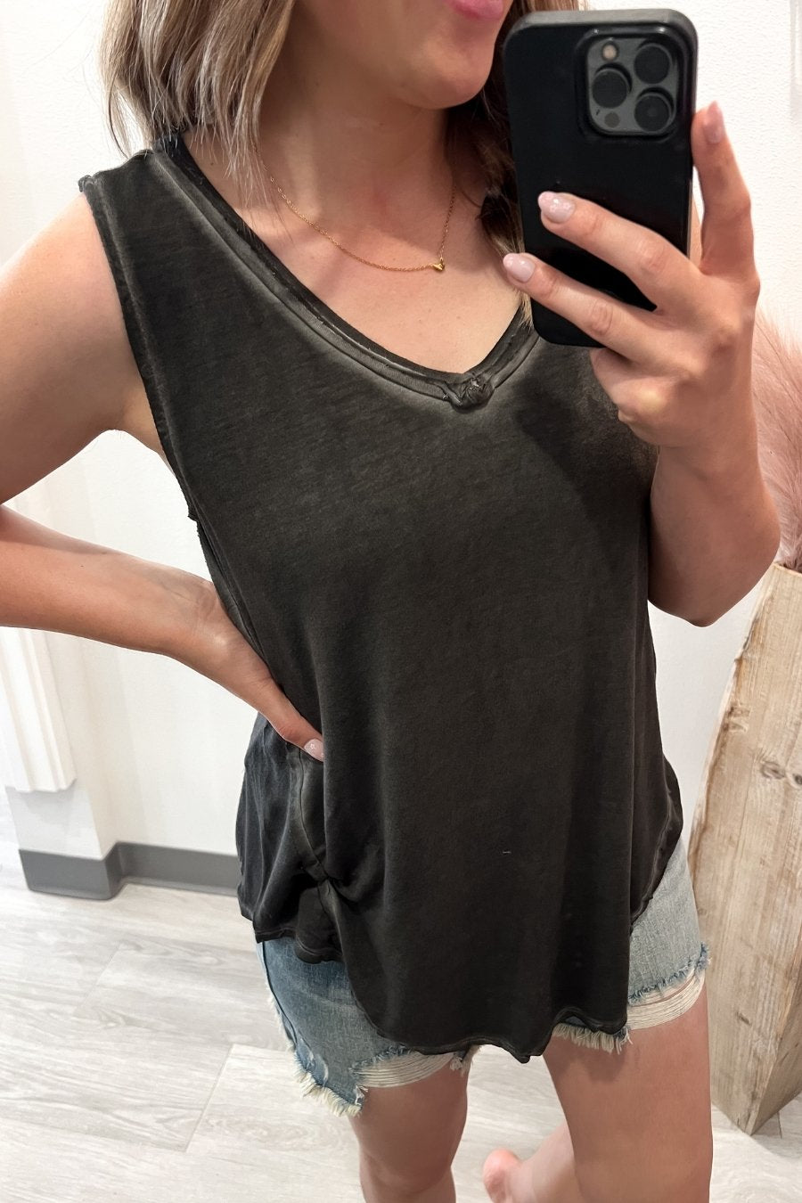 Person wearing a black sleeveless top and denim shorts, holding a phone.