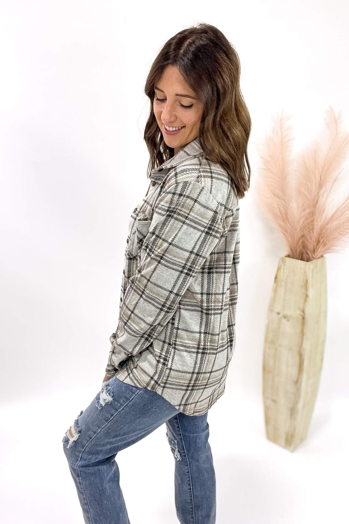 Woman wearing a plaid shirt and jeans standing next to a decorative vase with dried plants on a white background