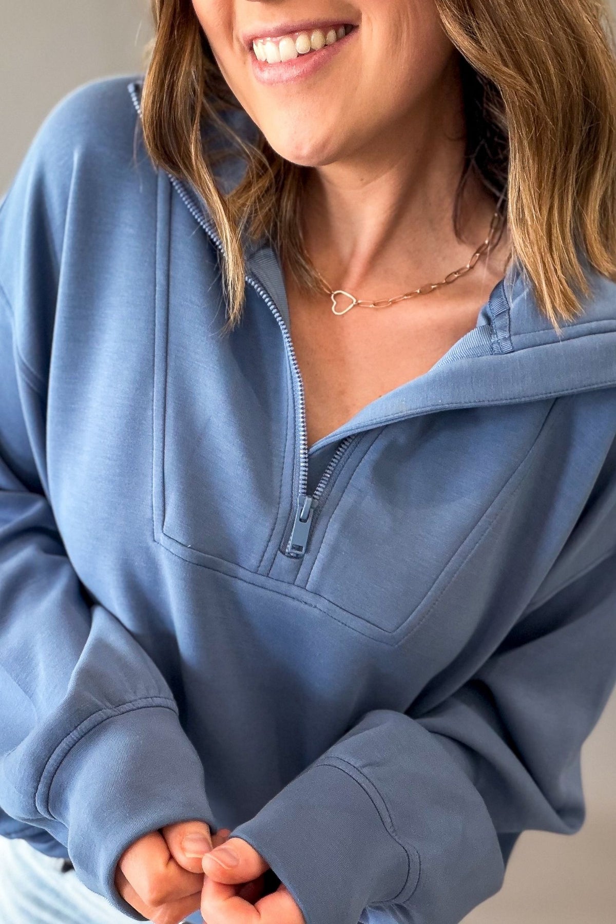 woman wearing a blue mock neck quarter zip pullover on a grey background showing the details