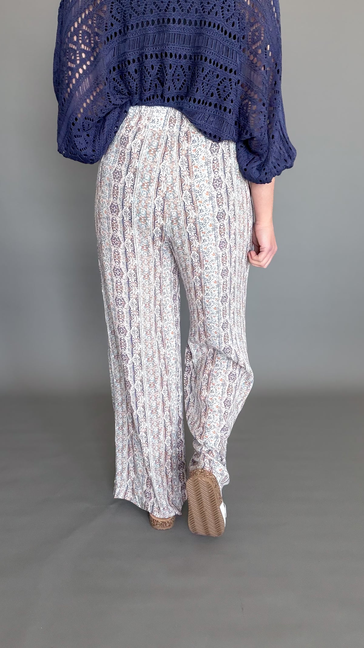 Person wearing a blue knitted top and white patterned pants on a gray background showing the back details.