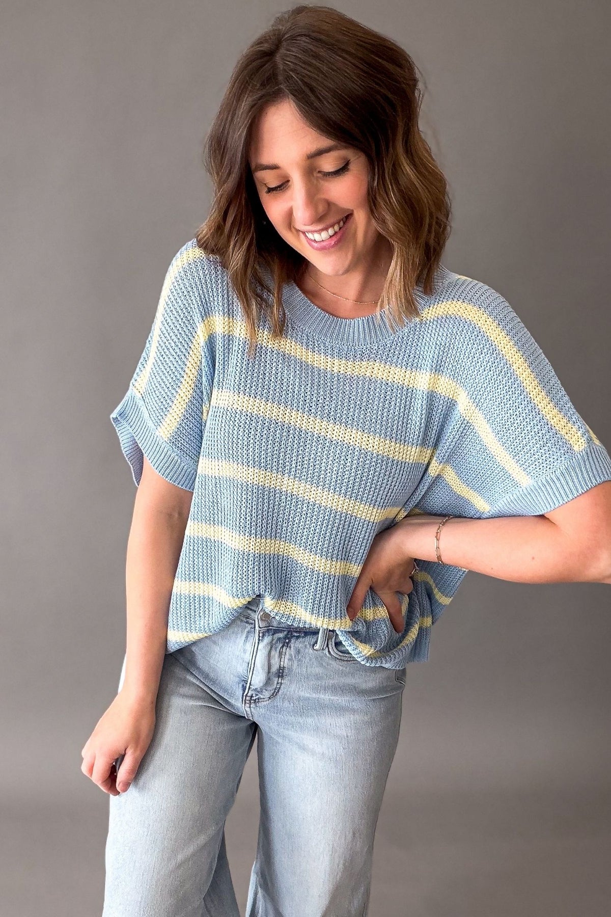 Woman wearing a blue and yellow knit striped sweater against a gray background