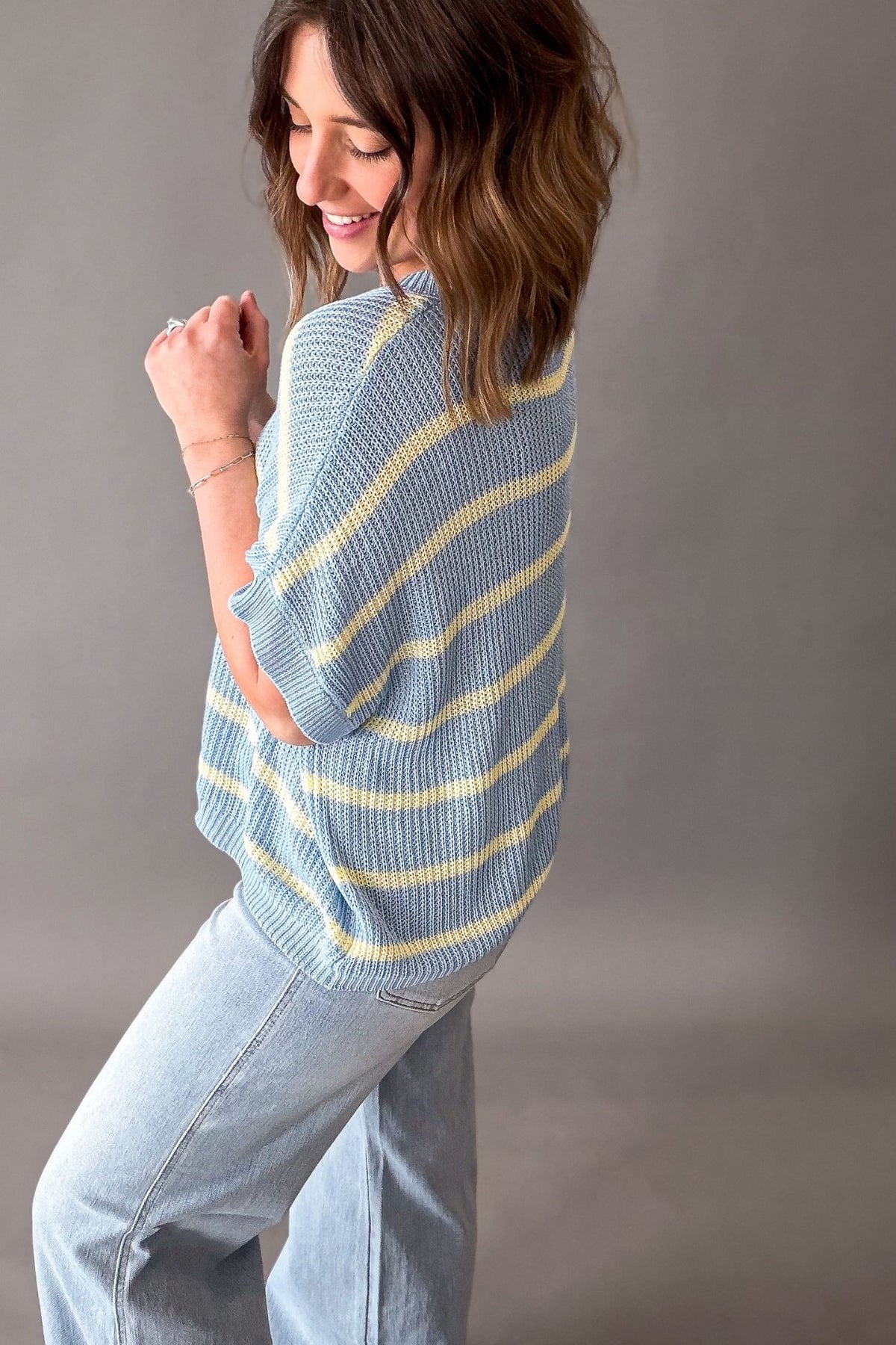 Woman wearing a blue and yellow striped sweater against a gray background showing the side and back details