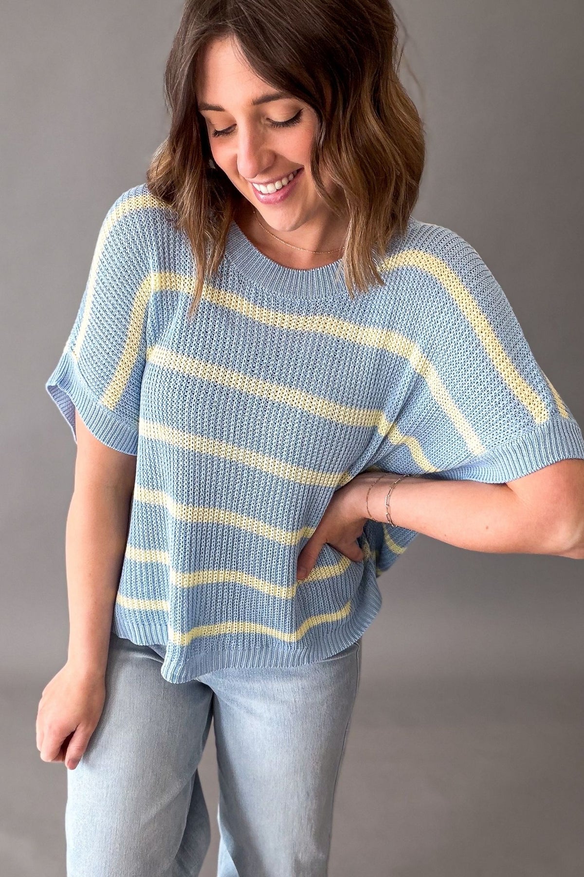 Woman wearing a blue and yellow striped short sleeve sweater against a gray background