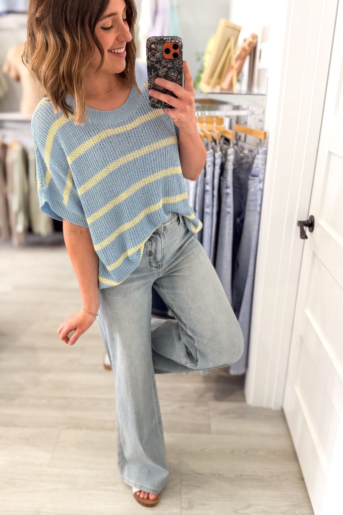 Woman taking a selfie in a clothing store wearing a striped short sleeve sweater, jeans and white slides.