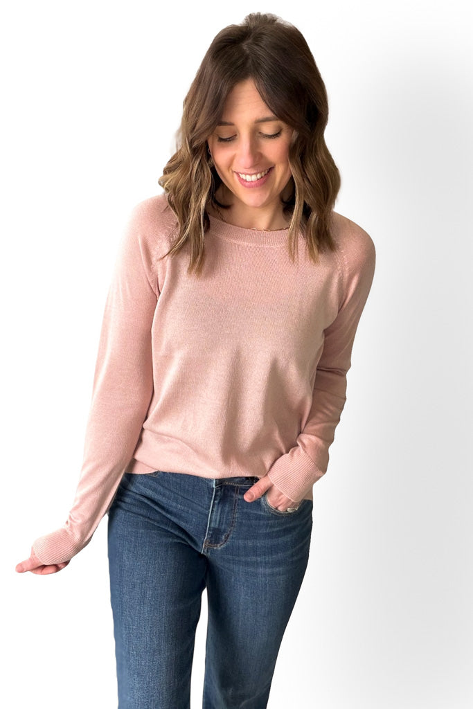Woman wearing a blush sweater and blue jeans on a white background