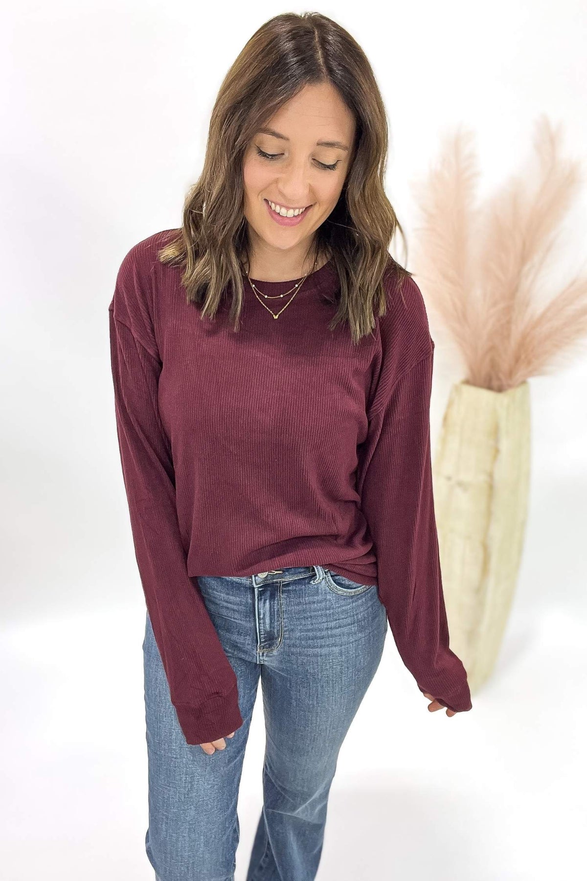 Woman wearing a burgundy long-sleeve top and blue jeans against a white background
