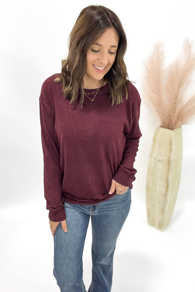 Woman wearing a burgundy long-sleeve top and blue jeans against a white background