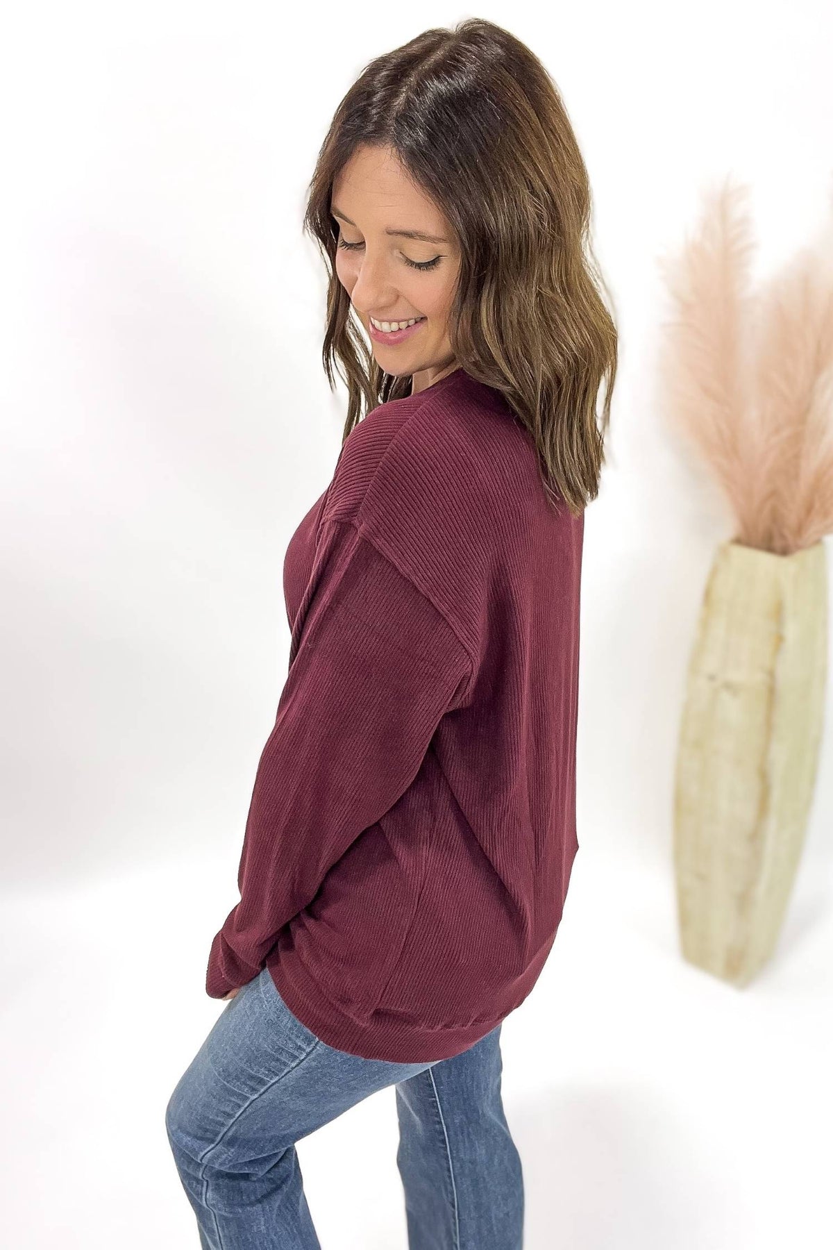 Woman wearing a burgundy sweater and blue jeans against a white background