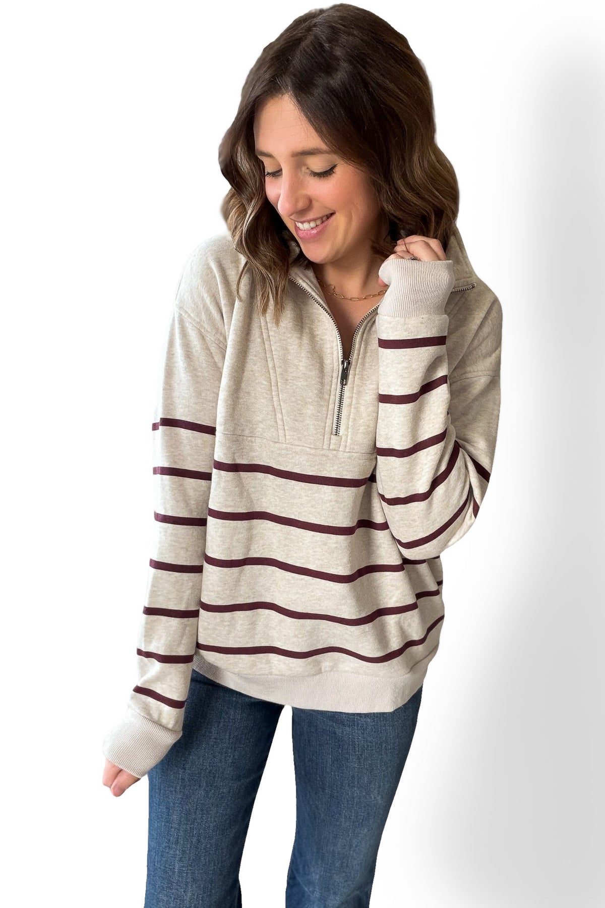 Woman wearing a beige and burgundy half zip striped sweater on a white background