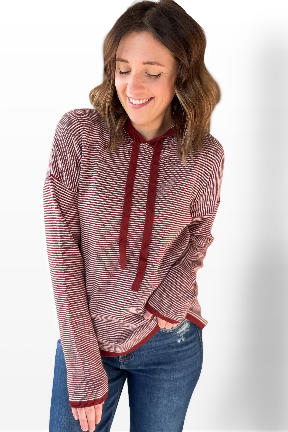 Woman wearing a burgundy and white striped hoodie with blue jeans on a white background