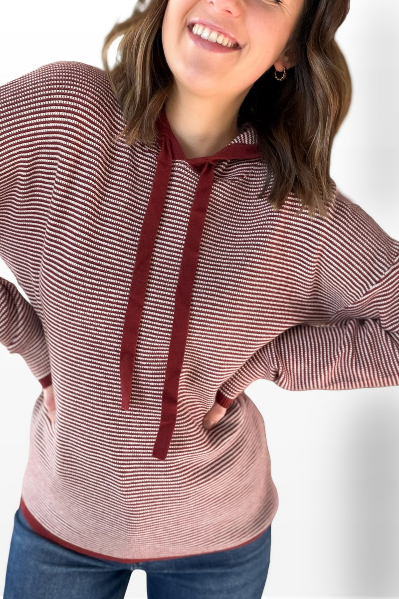 woman wearing a burgundy and white hoodie with blue jeans with a white background