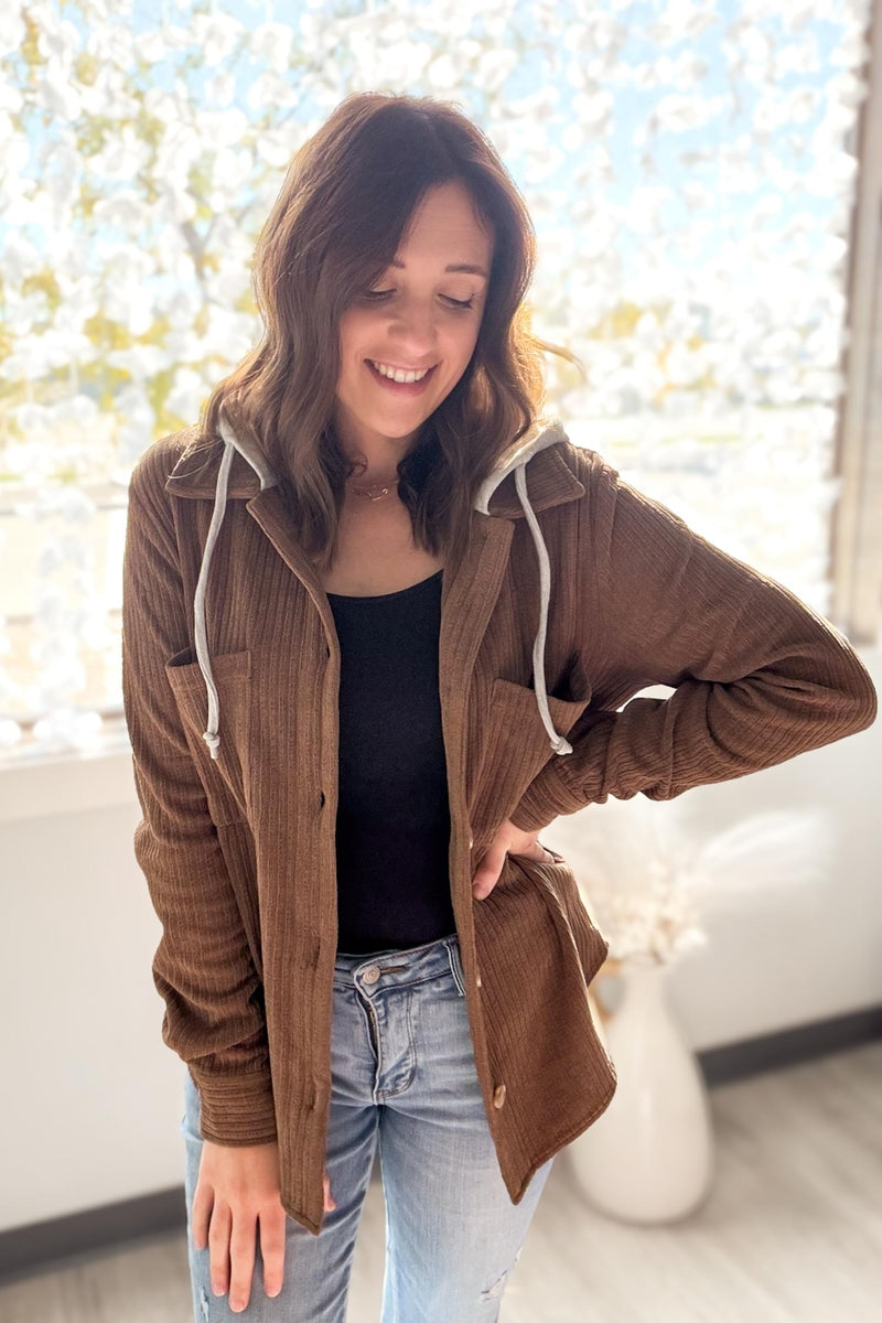 Woman wearing a brown/camel jacket and blue jeans indoors with a blurred background