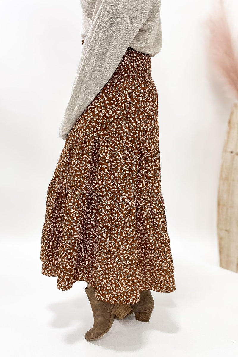 Person wearing a camel floral skirt with a plain background
