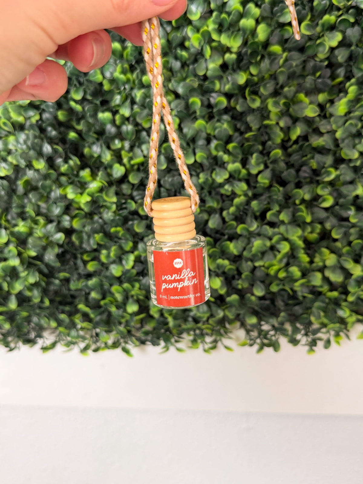 Small glass bottle with wooden cap labeled 'vanilla pumpkin' against a green leafy background.